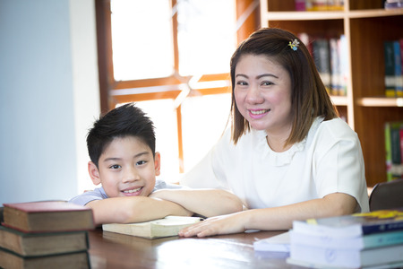 52374315 - portrait of happy boy and teacher reading book by bookshelf in library